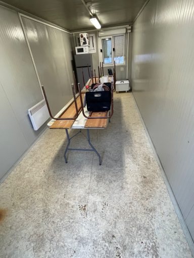 Intérieur d'un conteneur avec une table renversée et des murs gris, sol sale.